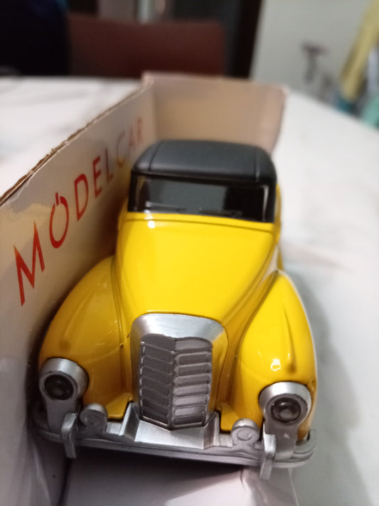 A vintage-style yellow model car toy with a black roof and silver grille, photographed inside its cardboard box. The box has the word 'MODEL CAR' printed in red on the side.