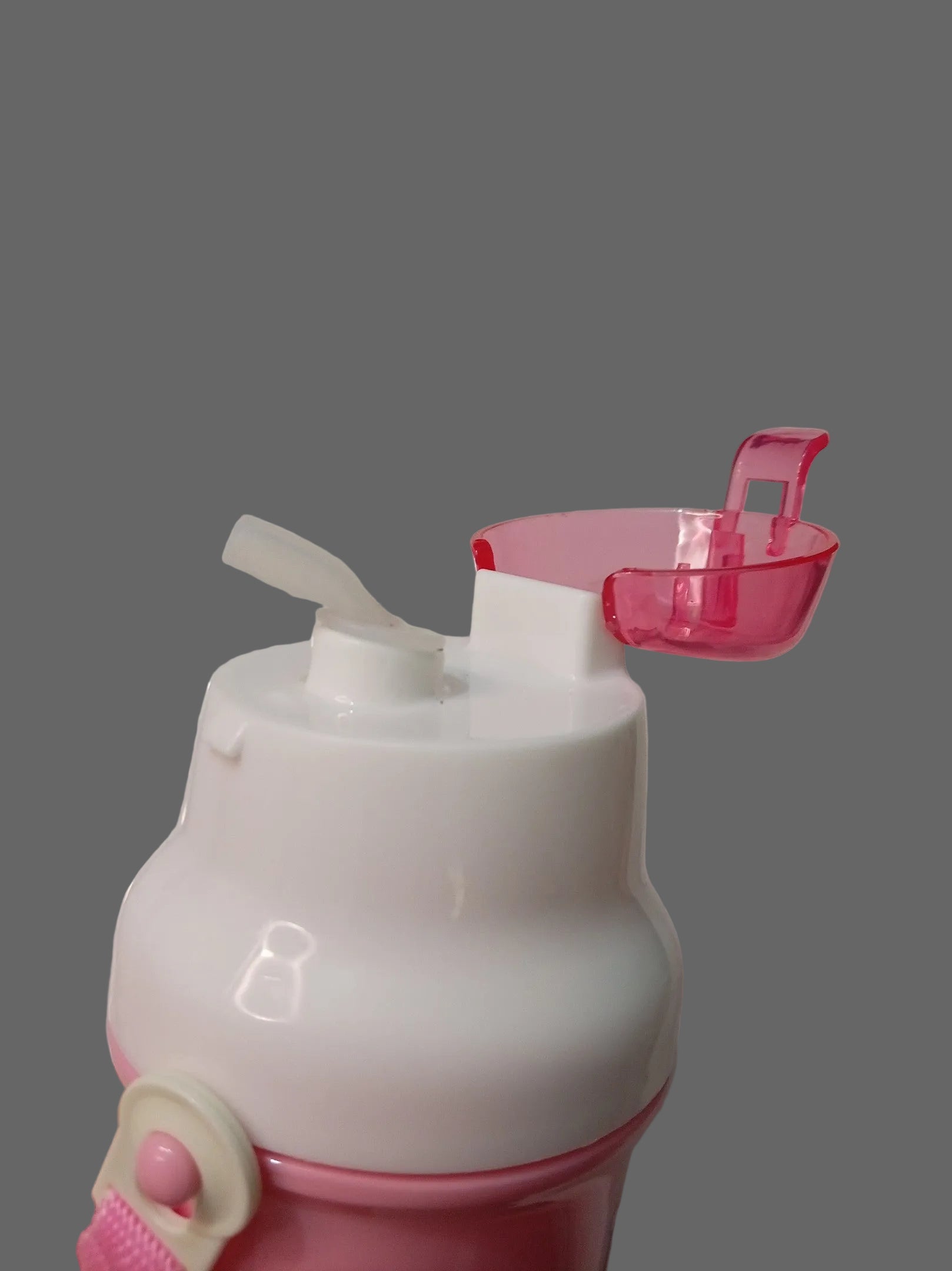 A close-up of a pink and white plastic water bottle with a flip-top lid and a small translucent pink cup attached above it, resting on a white marble surface.