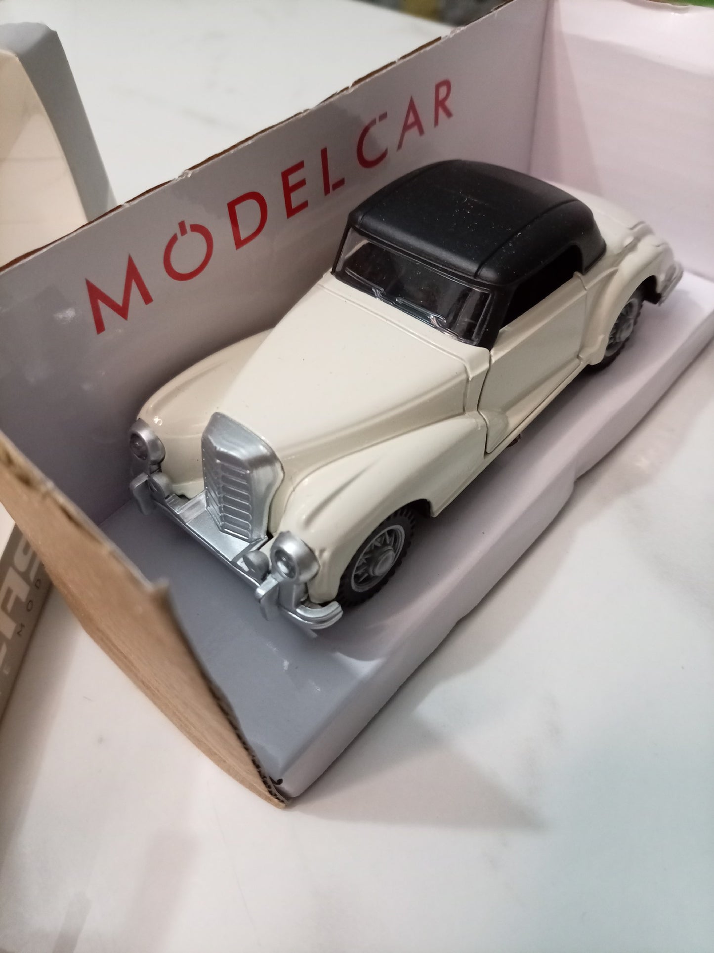 A vintage-style model car in a cream body with a black roof, displayed inside its open retail box. The box interior shows the red text 'MODEL CAR'.