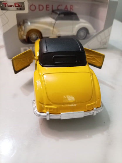 A yellow vintage model car with a black roof and open doors, shown from the rear, with its retail packaging box in the background.